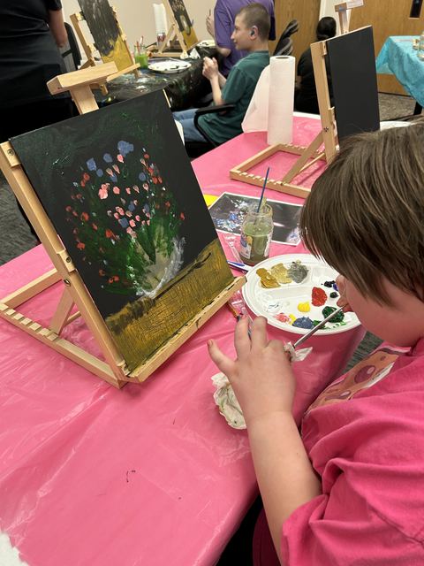 An artist painting a bouquet of flowers at a table easel