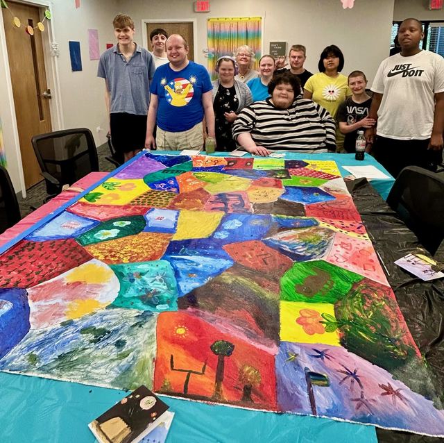 Joyful Arts artists gathered around a large, brightly colored group painting they created together