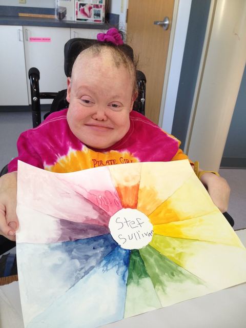 Stef Sullivan smiling, holding one of her colorful paintings