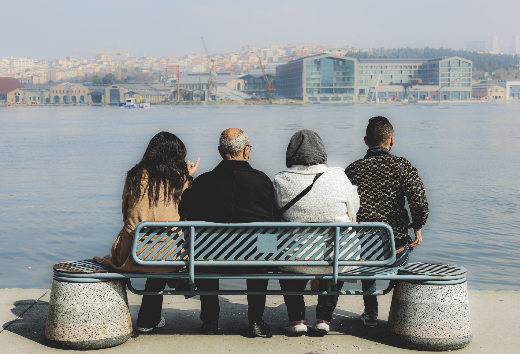 Un grupo de amigos sentados juntos en una banca junto al río, disfrutando de una vista panorámica del agua.