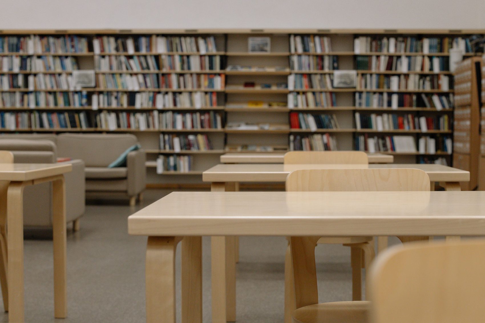 Un interior moderno de biblioteca con mesas de madera, sillas y estanterías llenas de libros.