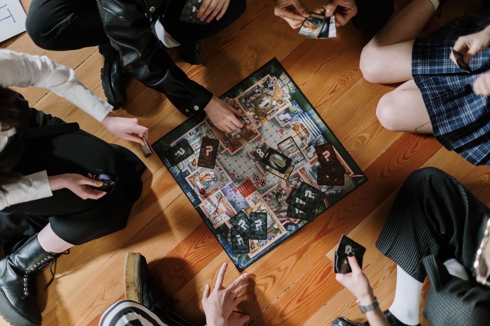 Visto desde arriba, un grupo de amigos extiende las manos sobre un juego de mesa en un piso de madera