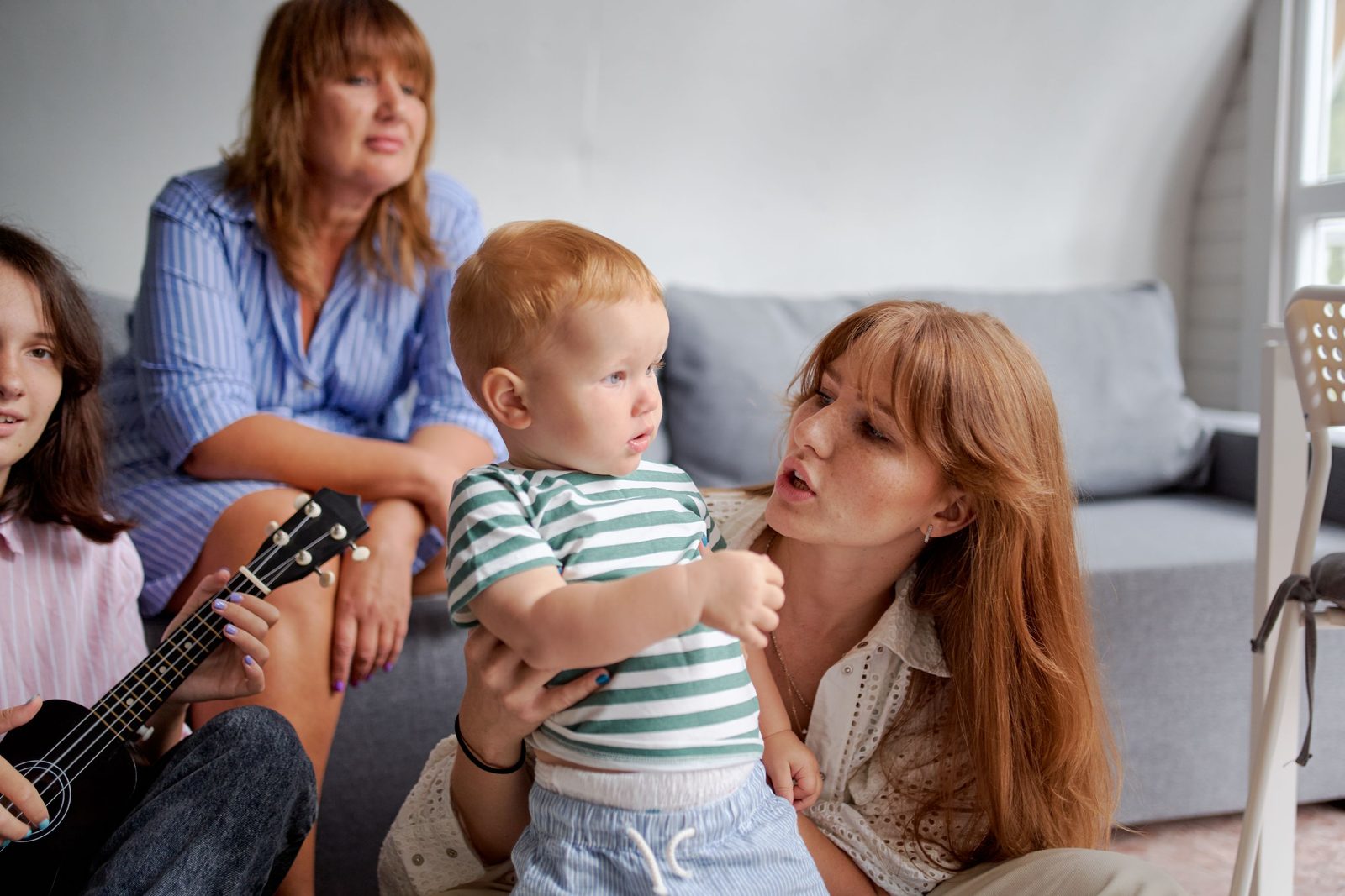 Cuidadores sentados juntos con niños pequeños en el regazo mientras uno toca un ukelele